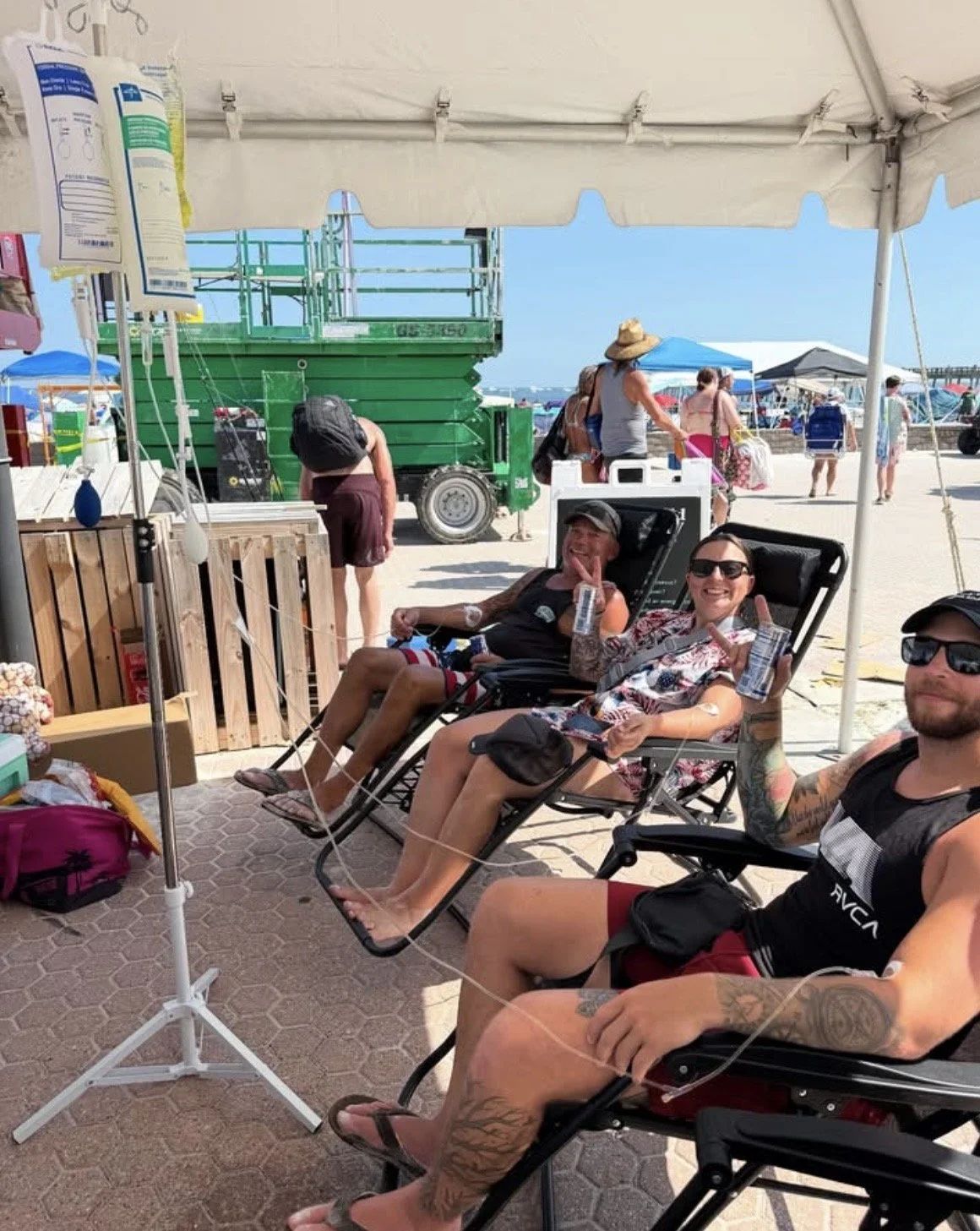 A group receiving IV therapy under a shaded tent at a beach event